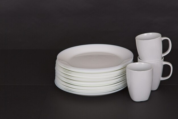 Closeup shot of white plates and mugs on a black background