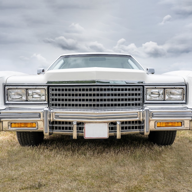 Closeup shot of a white retro car parked on a dry field under a cloudy sky