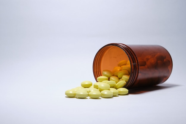 Closeup shot of yellow tablets fallen out brown bottle on white background