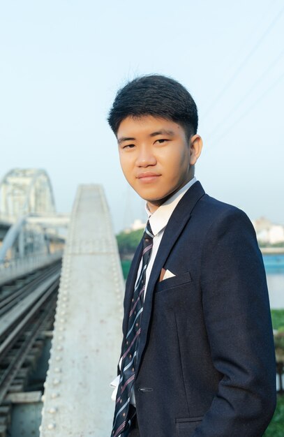 Closeup shot of a young Asian man in a suit standing on a bridge