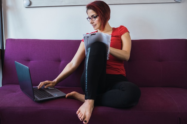 Free photo closeup shot of a young beautiful woman writing and sitting on the sofa in front of the laptop