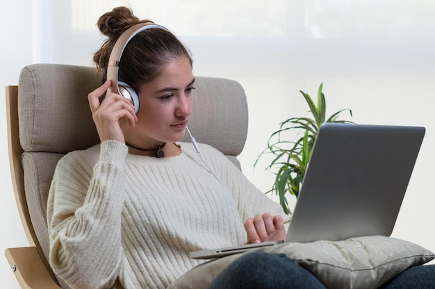 Closeup shot of a young european woman using a laptop with headset sitting on the chair at home