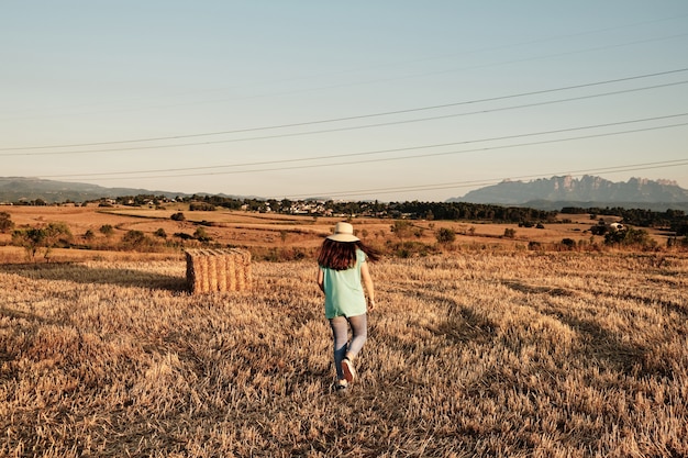 Closeup shot of a young girl with a round hat walking in the field