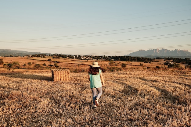 Снимок крупным планом молодой девушки в круглой шляпе, идущей в поле
