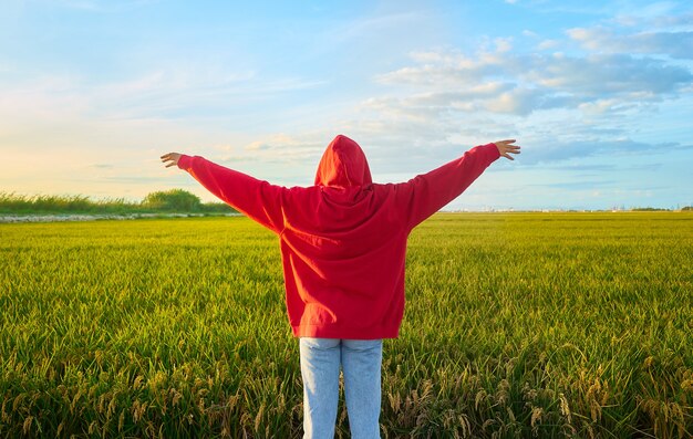 Снимок крупным планом молодой женщины в красном, весело стоящей в зеленом поле в солнечный день