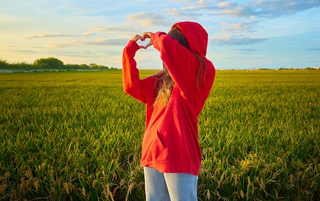 Closeup shot of a young lady in red  cheerfully standing in a  green field on a sunny day