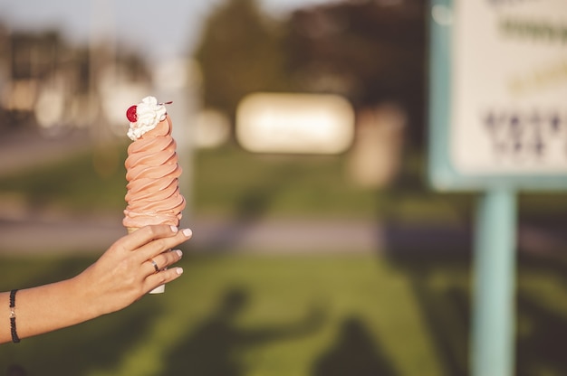 Крупным планом вид сбоку женщины, держащей высокий рожок мороженого