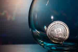 Foto gratuita primo piano di un bitcoin d'argento su una superficie riflettente blu in un bicchiere e l'istogramma della valuta