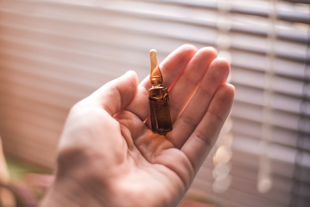 Closeup of a small ampoule on a hand under the sunlight with a window on a blurry background