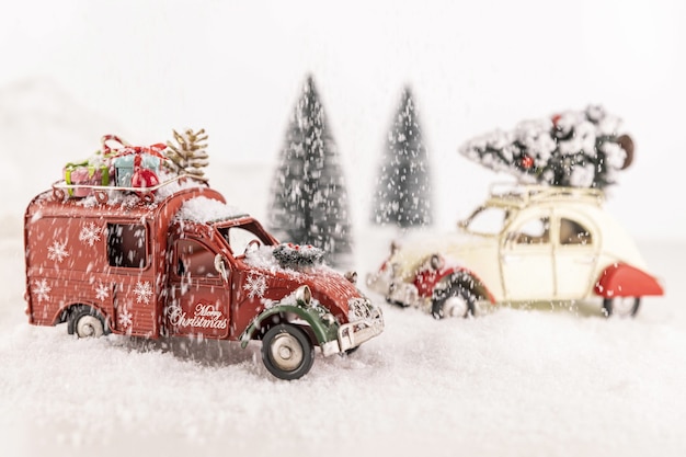 Closeup of small car toys on artificial snow with small Christmas trees on the background