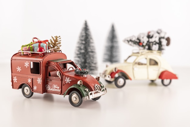 Closeup of small toy cars on the table with small Christmas trees in the background