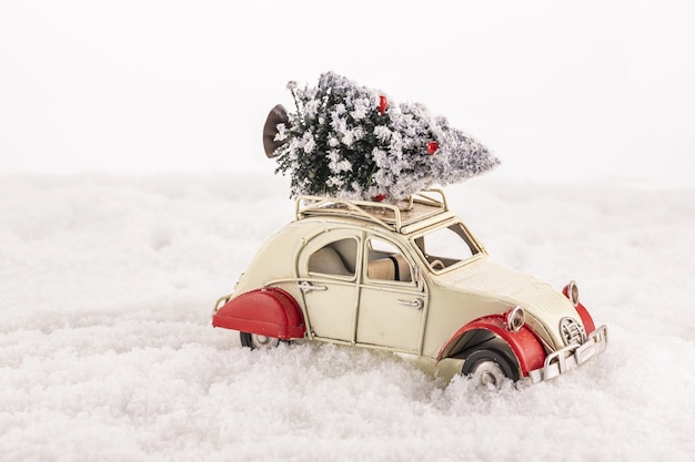 Closeup of a small vintage toy car with a Christmas tree on its roof on an artificial snow