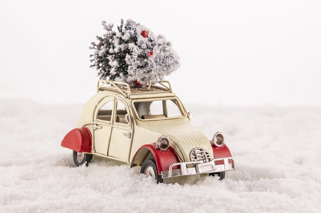 Closeup of a small vintage toy car with a Christmas tree on its roof on snow