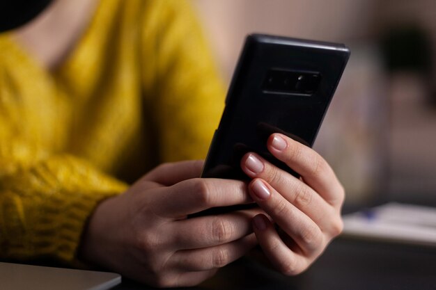 Closeup of social media vlogger with headset holding smartphone reading questions answering using production microphone sitting at desk in podcasting studio at home. On-air show