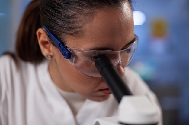 Closeup of specialist researcher analyzing blood sample using medical microscope working at vaccine development during biochemical experiment in hospital laboratory. Medicine investigation