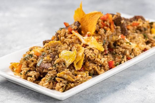 Крупный план острого вареного риса с мясом, овощами и чипсами в тарелке на столе