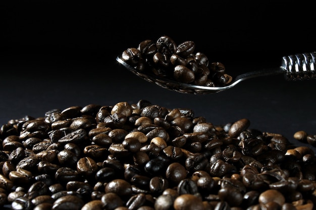Closeup of a spoon holding freshly roasted coffee beans against a dark background