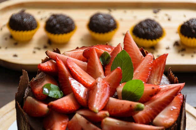 Closeup of strawberries with basil leaf and blackberry jam, on the chocolate cake, with chocolate plates around it. in the background brigadier (brazilian sweet).