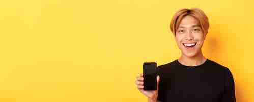 Free photo closeup of stylish handsome korean guy showing smartphone screen and smiling pleased recommend mobil