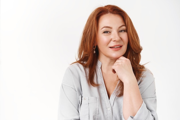 Closeup stylish successful goodlooking confident redhead middleaged businesswoman hold hand under faceline smiling amused curious listening interesting conversation white background