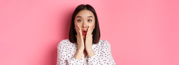 Free photo closeup of surprised and amazed asian woman staring at camera gasping impressed holding hands near m