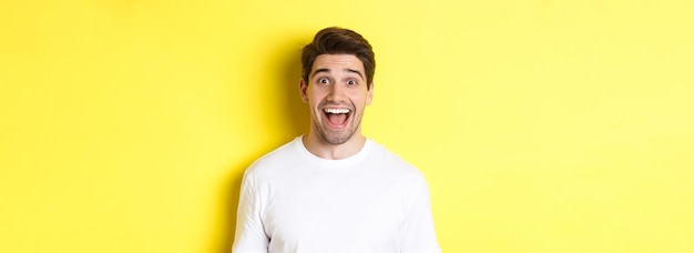 Free photo closeup of surprised handsome guy reacting to great news standing over yellow background in white