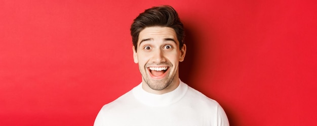 Closeup of surprised happy guy in white sweater looking amused hear interesting news standing over r...