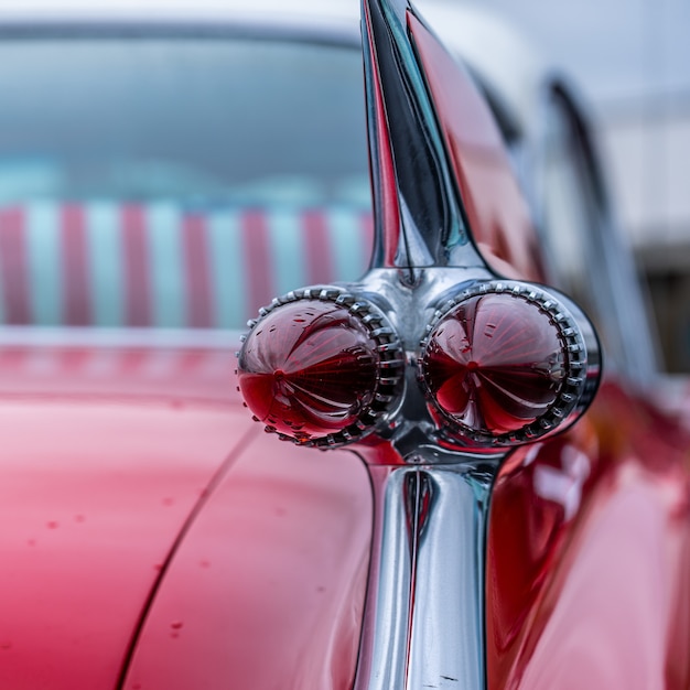 Closeup of the tail light of a red vintage car parked outdoors during the rain