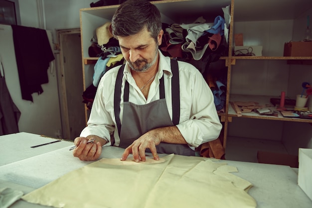 Closeup of tailors table with male hands tracing fabric making pattern for clothes in traditional atelier studio. The man in female profession. Gender equality concept