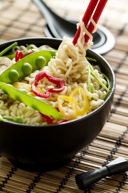 Closeup of tasty appetizing asian noodles soup with vegetables in black ceramic bowl. Closeup. 