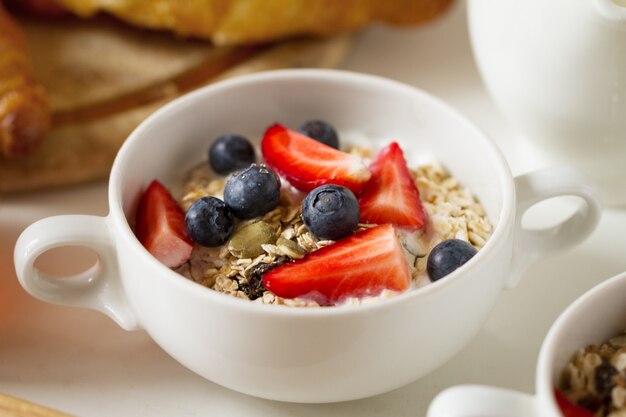 白いボールでオートミール、フルーツ、ヨーグルトとおいしい食欲をそそぐmuesliの拡大写真。朝の健康食品のコンセプト。