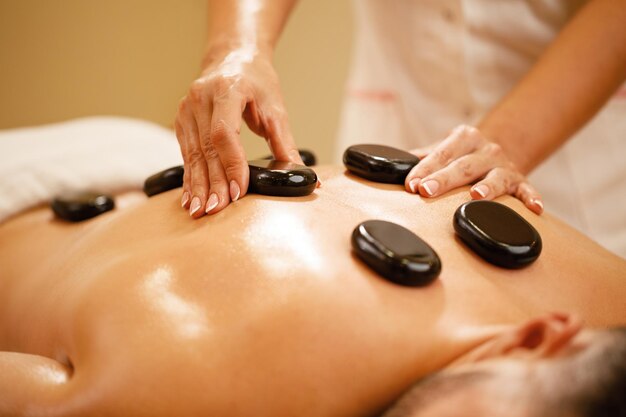 Closeup of therapists placing hot stones on man's back during lastone therapy at the spa