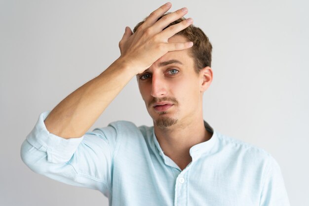 Closeup of tired disappointed blonde guy with face palm gesture. 