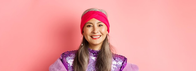 Closeup of trendy asian senior woman with grey hair and stylish disco dress smiling happy at camera