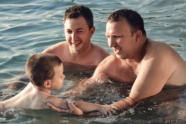 Closeup of two  Caucasian men teaching a young boy to swim