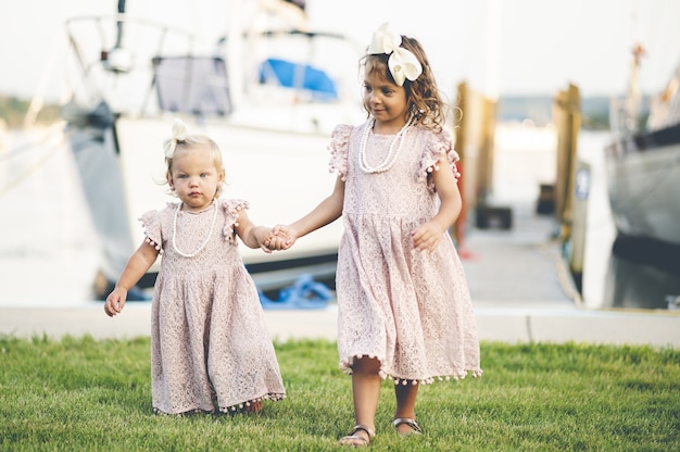Closeup of two cute baby girls in similar dresses walking near the harbor