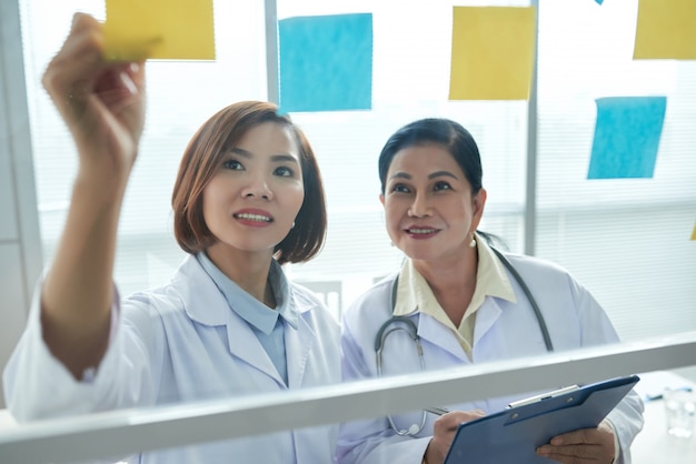 Free photo closeup of two medical workers putting memo stickers on the glass board