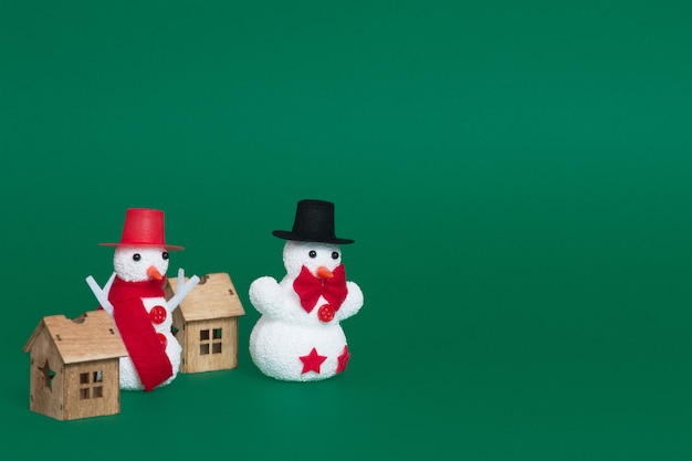 Крупным планом двух снеговиков и небольших деревянных домиков как рождественские украшения на зеленом фоне