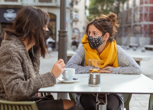 Closeup of two women wearing facemasks during the covid-19 pandemic, sitting at a cafe