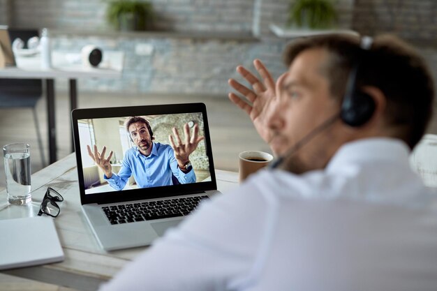 Closeup of uncertain businessman talking with his colleague during online meeting over a laptop