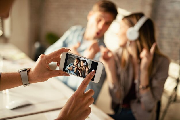 Closeup of unrecognizable woman taking a photo with smart phone of playful coworkers in the office