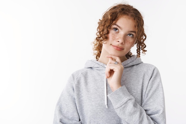 Free photo closeup unsure cute redhead teenage girl thinking look up dreamy thoughtfully touching chin deciding what wear college make choice standing doubtful white background relaxed everyday pose