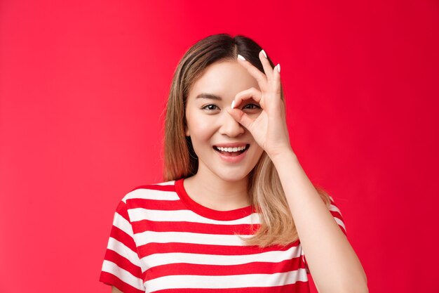 Closeup upbeat positive asian girl look through ok sign smiling broadly enjoy positive vibes judging...