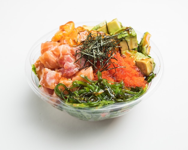 Closeup of a vegetable salad with avocados in a glass bowl on a white surface