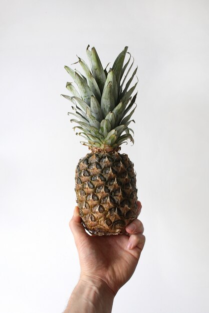 Closeup vertical shot of a person's arm holding a pineapple in hand on a white background