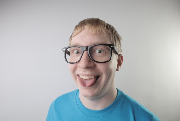 Closeup view of a caucasian male wearing a blue t-shirt and eyeglasses making funny face gestures