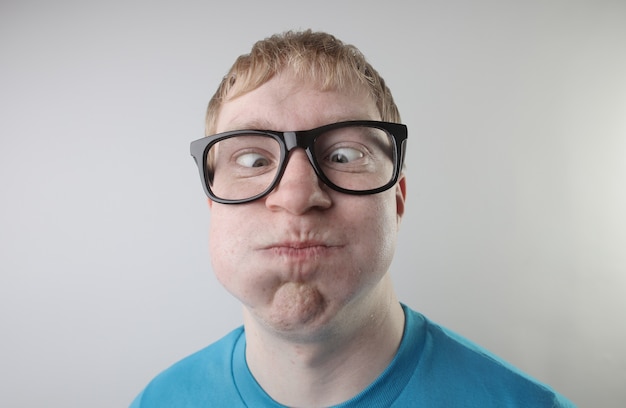 파란색 티셔츠와 재미 있은 얼굴 제스처를 만드는 안경을 착용하는 백인 남성의 근접 촬영보기