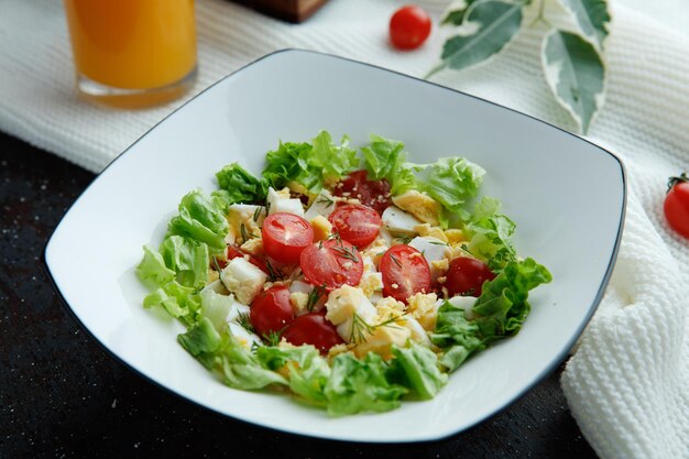 オレンジジュースと黒の背景の上の布に葉とプレートのトマト卵レタスと野菜サラダのクローズアップビュー