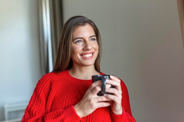 自宅の空白のスペースでホットドリンクのカップを持つ若い女性のクローズアップビュー人々の飲み物とレジャーの概念自宅でお茶やコーヒーのカップを持つ幸せな若い女性