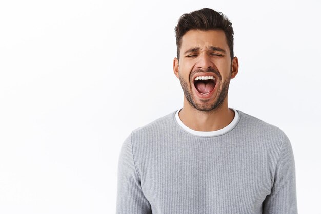 Closeup whining cute bearded hispanic guy screaming from pain or depression losing temper hate being surrounded problems shouting out loud open mouth wide while eyes close white background